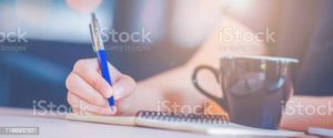 Woman hand is writing on a notebook with a pen in office.Web banner.